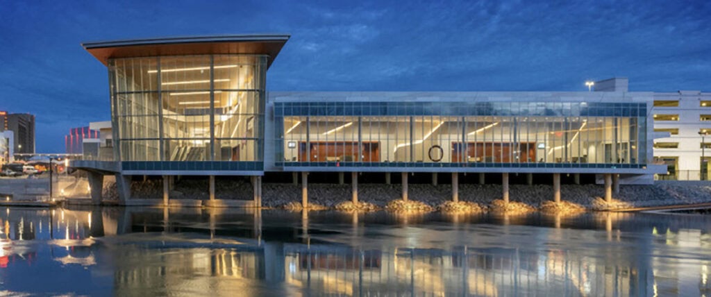 Modern glass building on stilts over water at dusk.