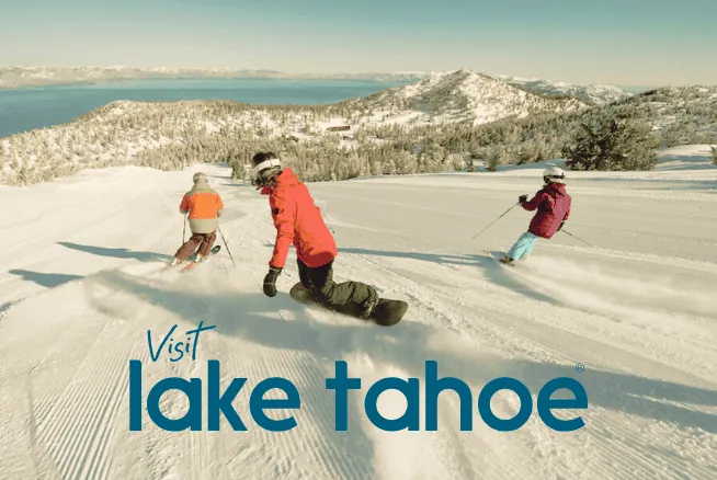 Three people skiing on snow-covered slopes with mountains in the background.