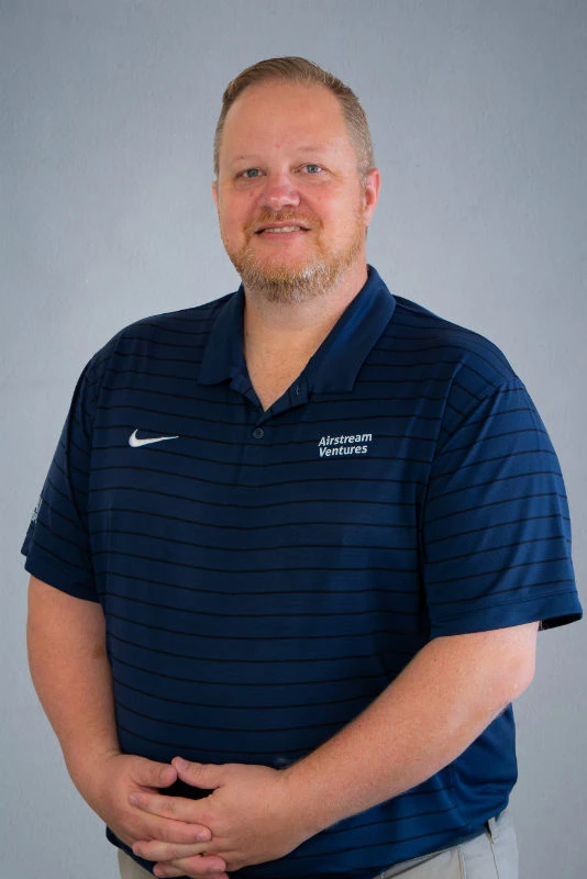Man in blue polo shirt with 'Austream Ventures' logo, smiling, against gray background.